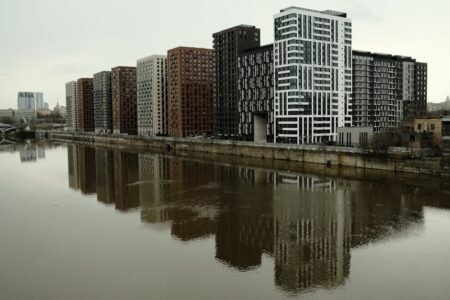 Captivating view of modern high-rise buildings reflecting in a calm river under cloudy skies.