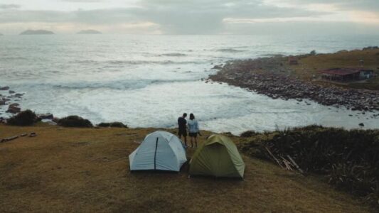 Two tents and a couple enjoying a scenic coastal view in Palhoça, Brazil.