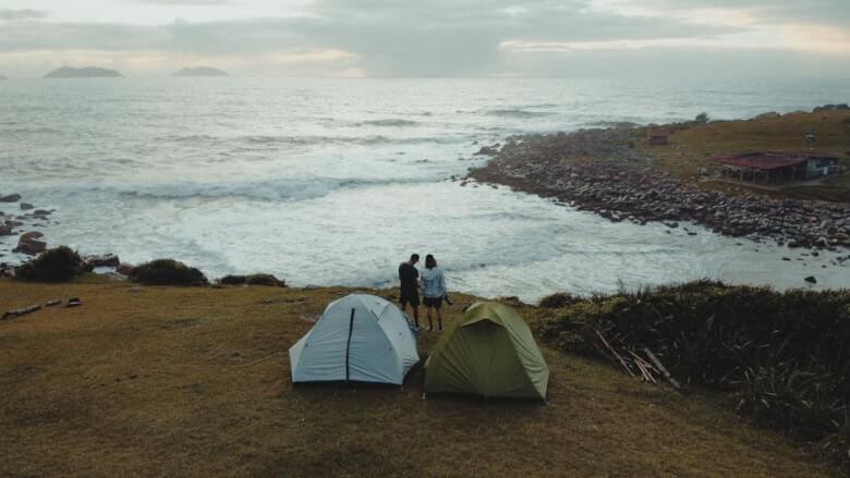 Two tents and a couple enjoying a scenic coastal view in Palhoça, Brazil.