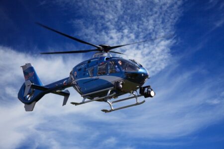 A blue police helicopter patrolling the sky on a clear sunny day.