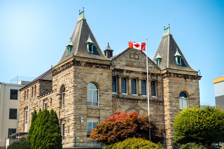 A classic stone courthouse in Nanaimo, British Columbia, with Canadian flag, under clear blue sky.
