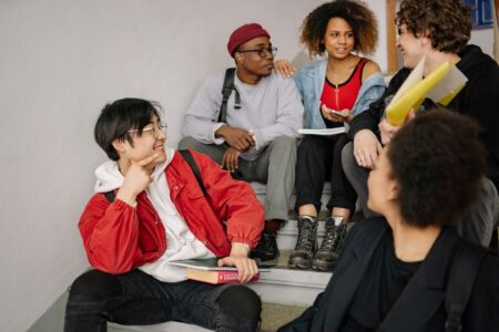 A diverse group of students sitting on stairs, smiling and collaborating indoors.