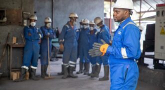 A group of factory workers in safety gear receiving training indoors.