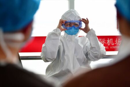 A healthcare professional dons protective clothing at an airport, highlighting safety measures during a pandemic.