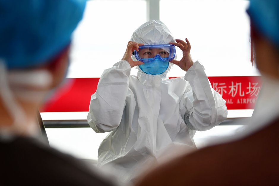 A healthcare professional dons protective clothing at an airport, highlighting safety measures during a pandemic.