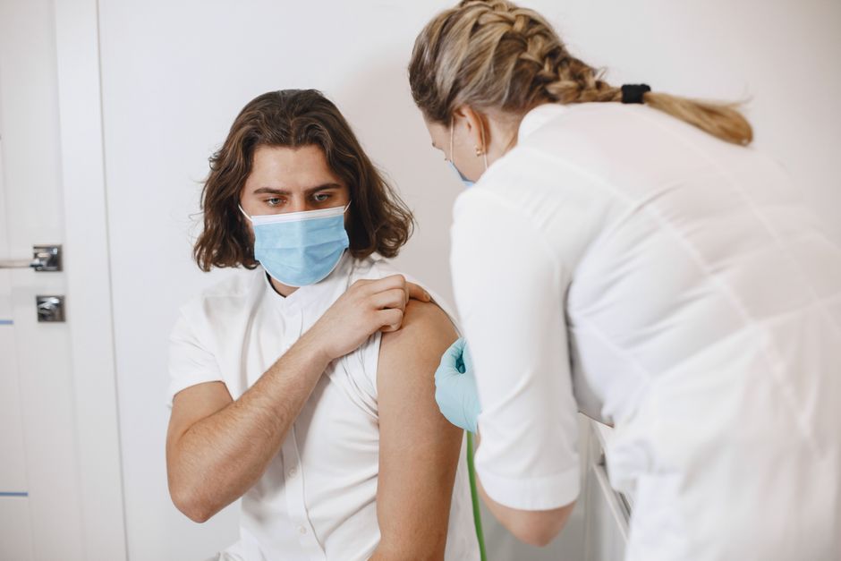 A healthcare worker wearing a mask gives a vaccine shot to a patient in a medical office.