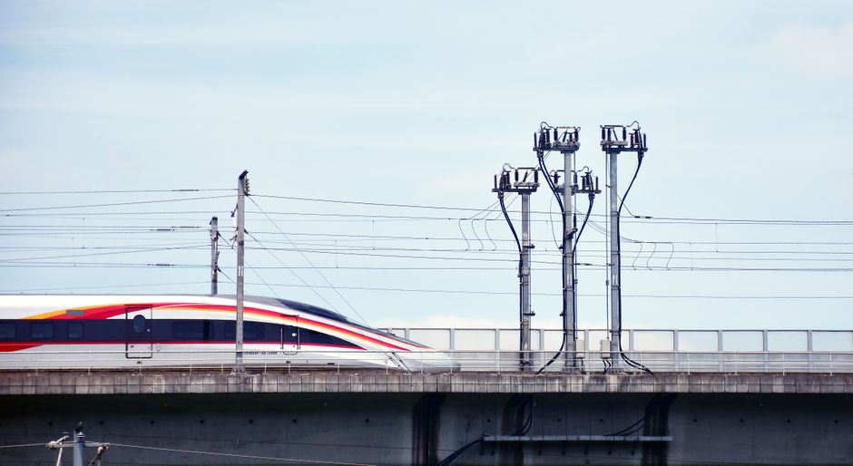 A high-speed train moves swiftly on an elevated railway under a clear sky.