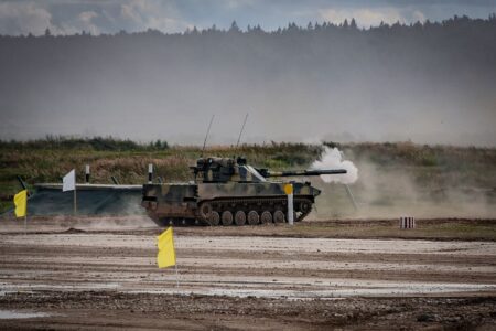 A military tank firing a shell during training in an open field.