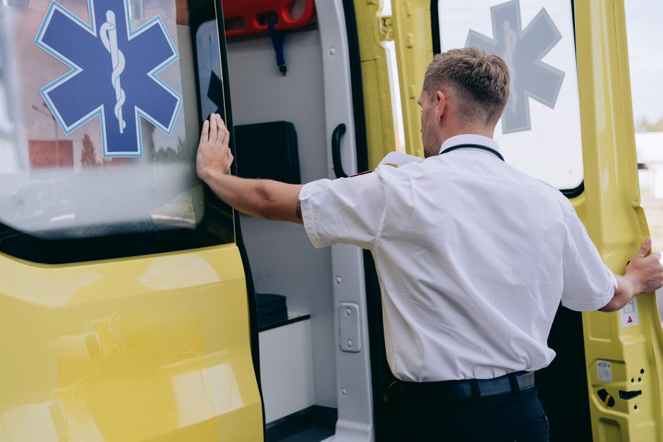 A paramedic in uniform opens the side door of a yellow ambulance during the day.