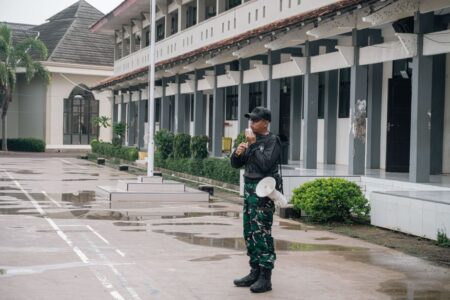 A security guard stands alert with a megaphone outside a building after rain.