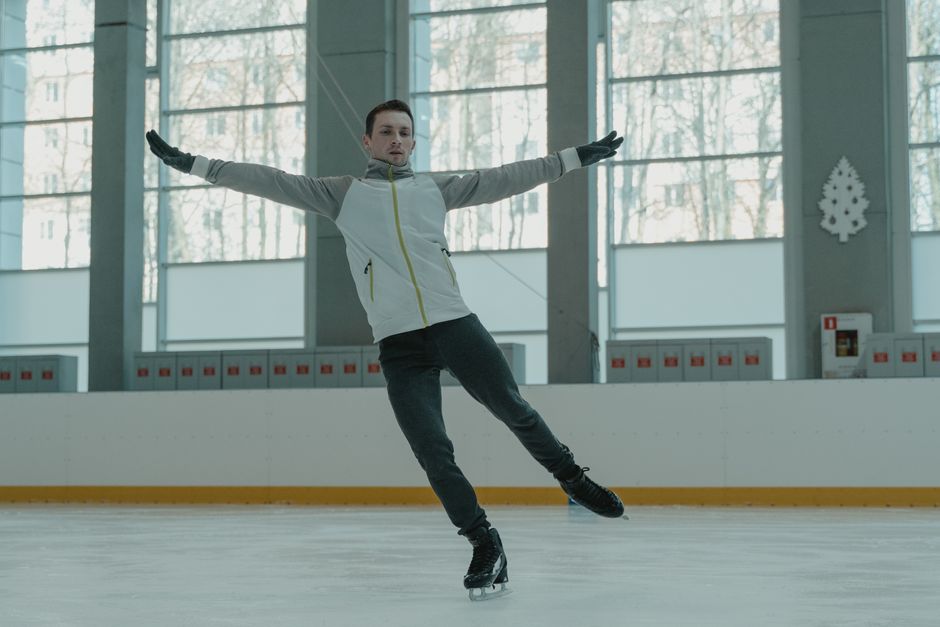 A skilled ice skater executing a graceful move indoors on a rink.