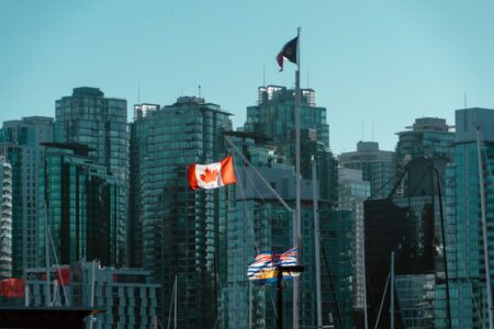 A view of Vancouver's glassy skyscrapers with Canadian and British Columbia flags waving in the foreground.