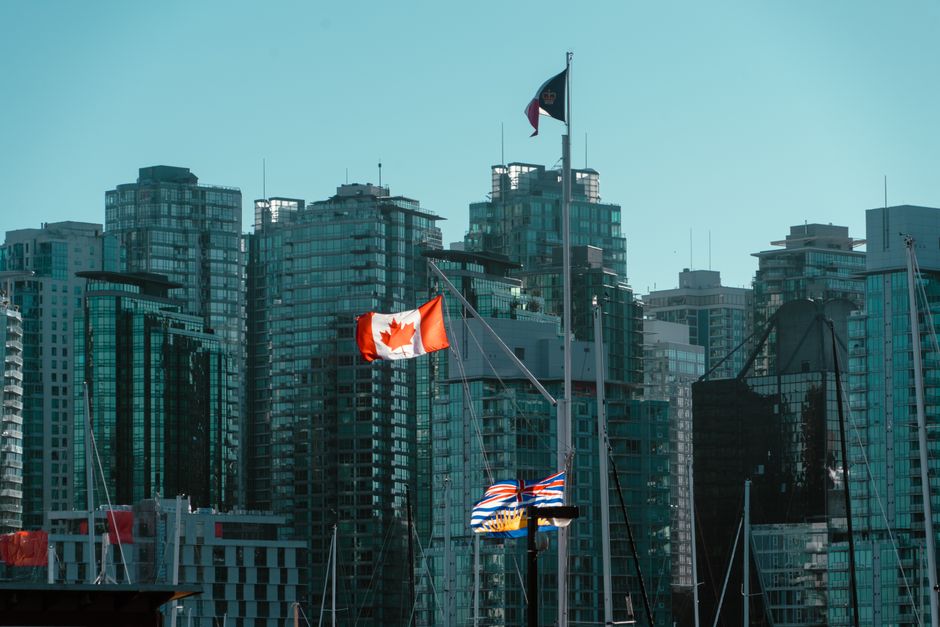 A view of Vancouver's glassy skyscrapers with Canadian and British Columbia flags waving in the foreground.