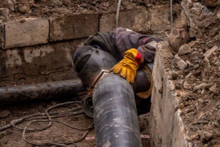 A worker welds a pipe in an urban trench, showcasing industrial construction work.