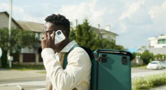 A young delivery man talks on his smartphone while carrying a thermal delivery bag outdoors.
