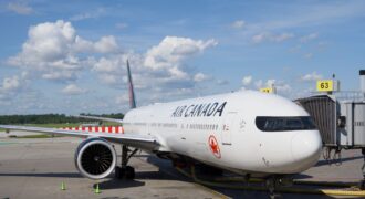 Air Canada Boeing 777 airplane parked at an airport gate under a clear blue sky.
