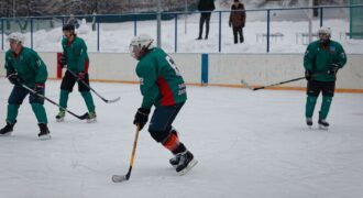 Amateur ice hockey match in snow-filled setting with players in green uniforms.