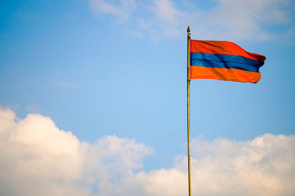 Armenian flag on a flagpole swaying in the windy blue sky with clouds.