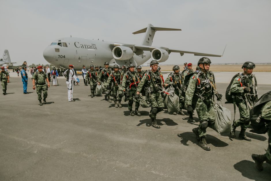 Canadian military paratroopers walk past a C-17 Globemaster on a sunny day at an airport.