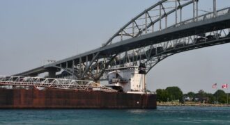 Cargo ship passing under the Blue Water Bridge connecting USA and Canada on a clear day.