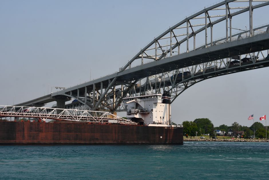 Cargo ship passing under the Blue Water Bridge connecting USA and Canada on a clear day.
