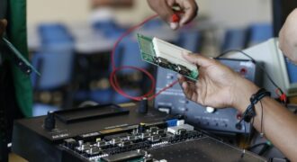 Close-up of hands working with electronics equipment and circuit board in a lab setting.