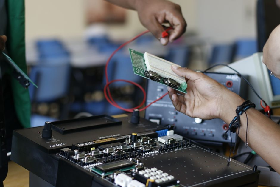 Close-up of hands working with electronics equipment and circuit board in a lab setting.