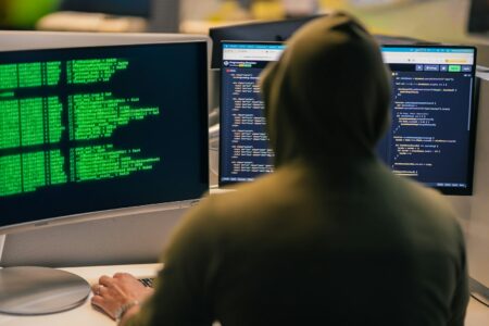 Хакер в капюшоне за несколькими мониторами