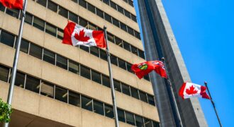 Flags of Canada and Ontario fluttering near the CN Tower under a clear blue sky in Toronto.