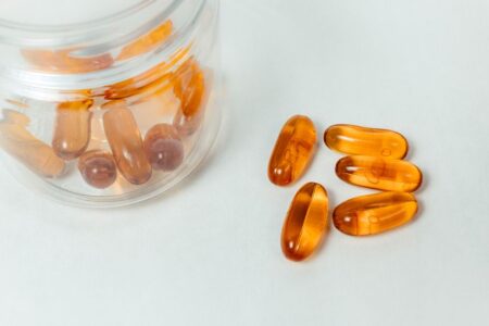 Glass container with amber capsules spilling out on a white background.