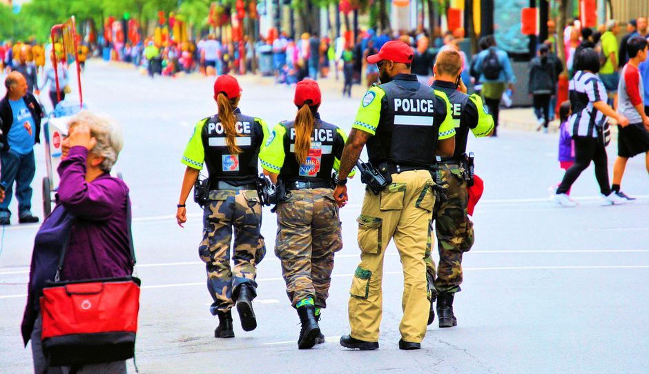 Group of police officers in uniform patrolling a crowded city street on a sunny day.