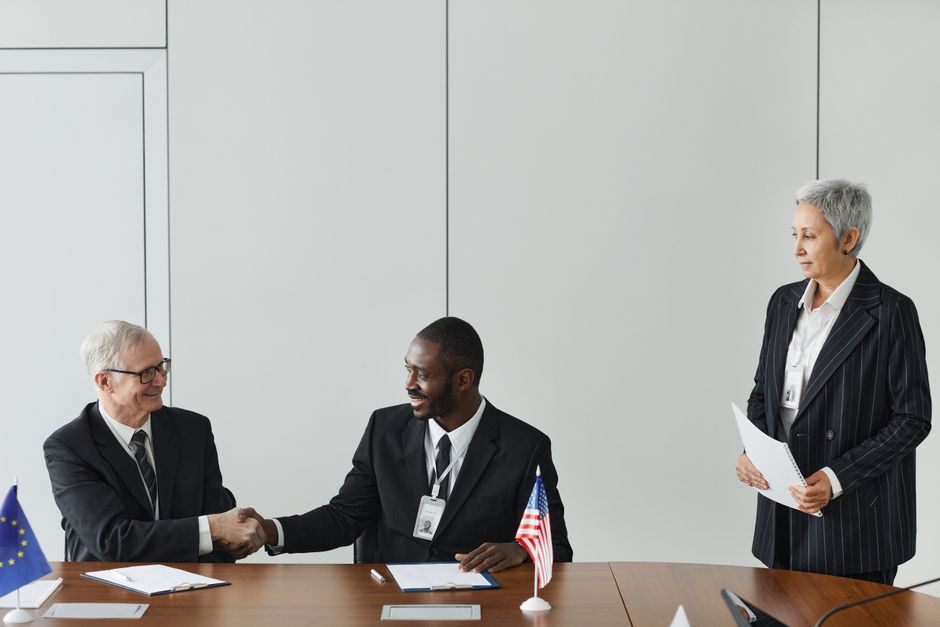 Multinational business meeting with agreement signing, featuring diverse professionals and flags.