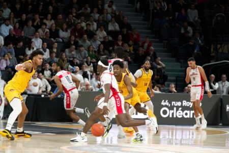 Players in action during an indoor basketball game, with a crowd watching intently.