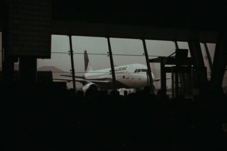 Silhouette of an airplane and waiting passengers inside an airport terminal at dusk.