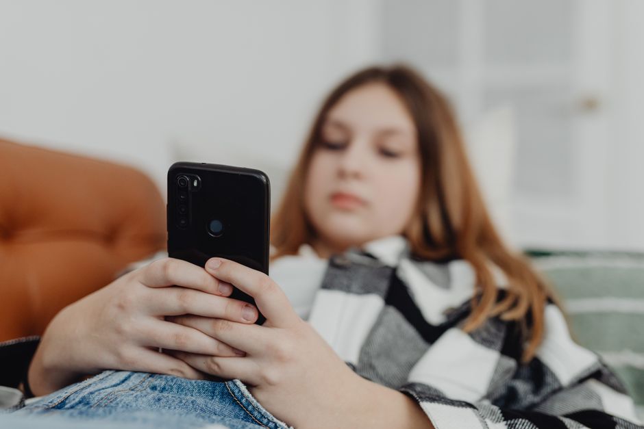Teenage girl using smartphone while relaxing on a sofa, depicting leisure and connectivity.