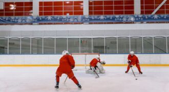 Three hockey players in red uniforms practicing on an indoor ice rink.
