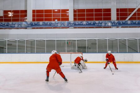 Three hockey players in red uniforms practicing on an indoor ice rink.
