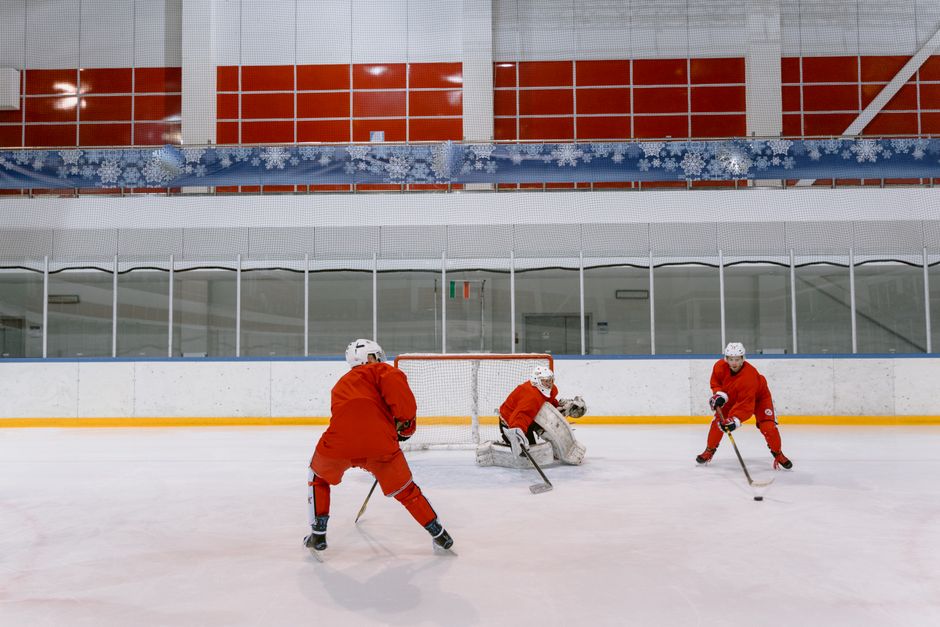 Three hockey players in red uniforms practicing on an indoor ice rink.