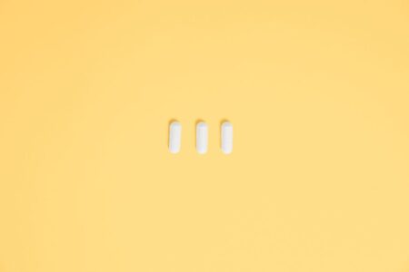 Three white capsules on a vibrant yellow background, symbolizing healthcare and medication.