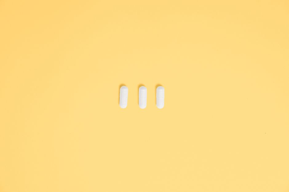 Three white capsules on a vibrant yellow background, symbolizing healthcare and medication.