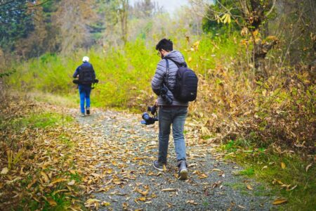 Two photographers walking down a leaf-covered forest path capturing nature's beauty.