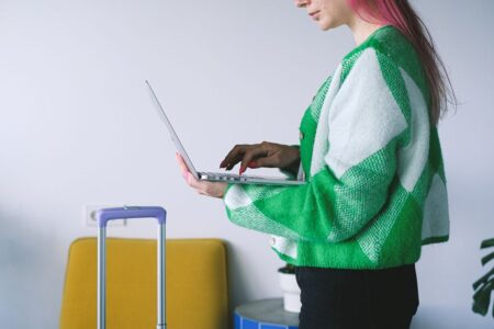 Young woman working on laptop near luggage in stylish hotel lounge, embracing the digital nomad lifestyle.